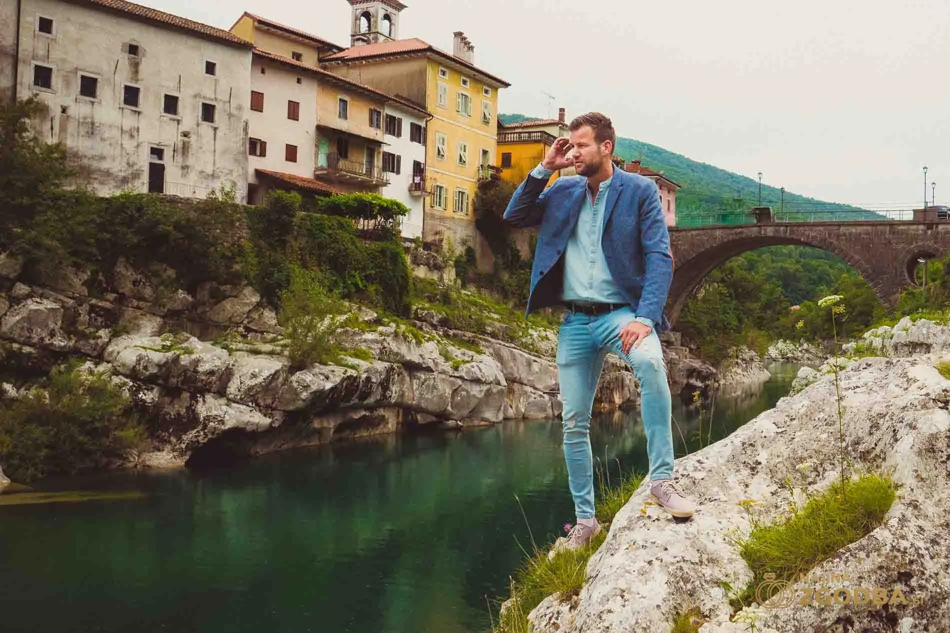 Primoz Lazar standing on rocks above a river, an old town behind him
