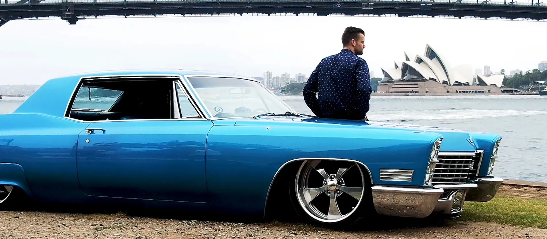 Primoz Lazar in Sydney, beside a classic blue car with the Opera House behind